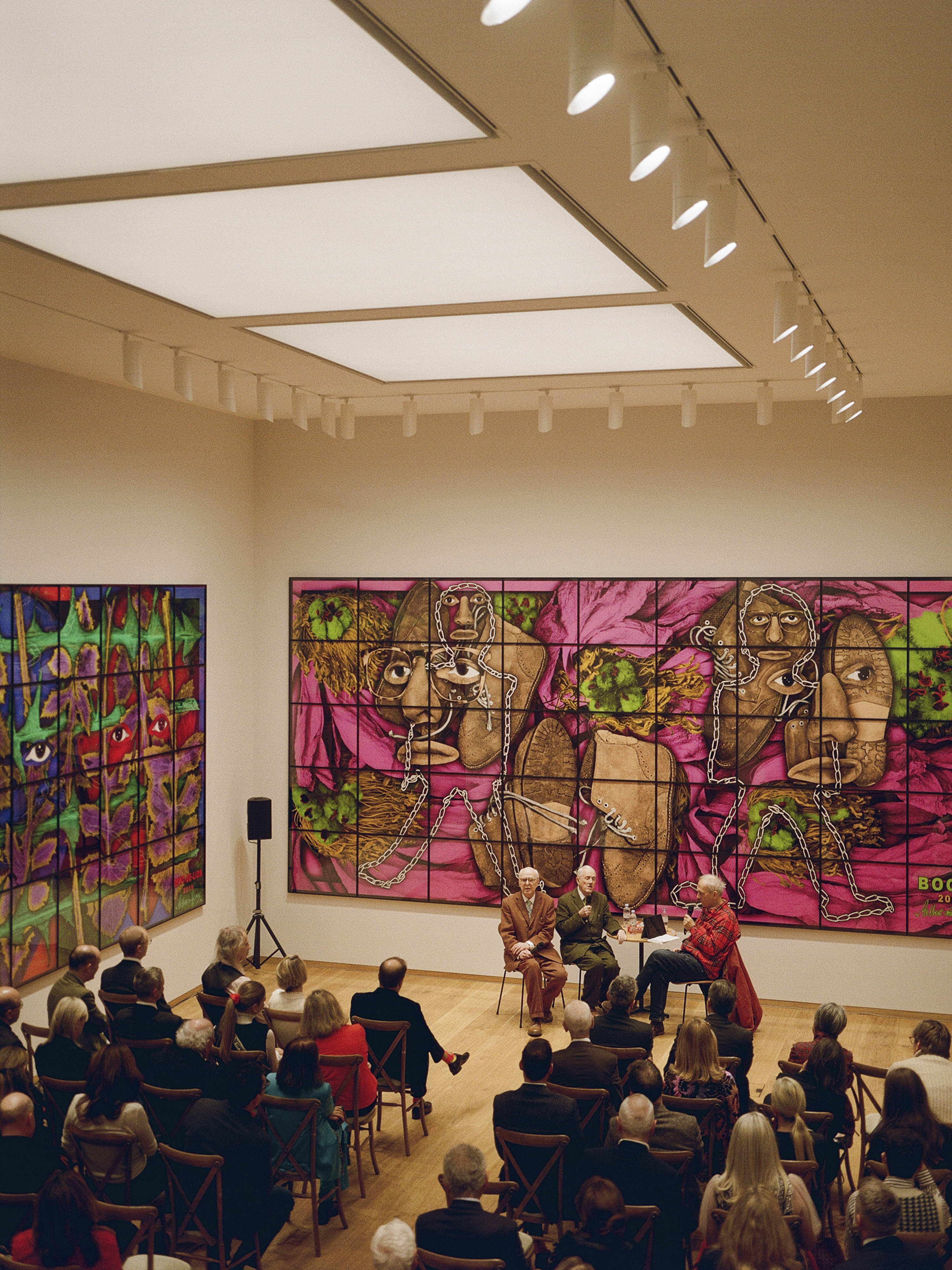 Gilbert and George give a talk in a gallery to a large audience.