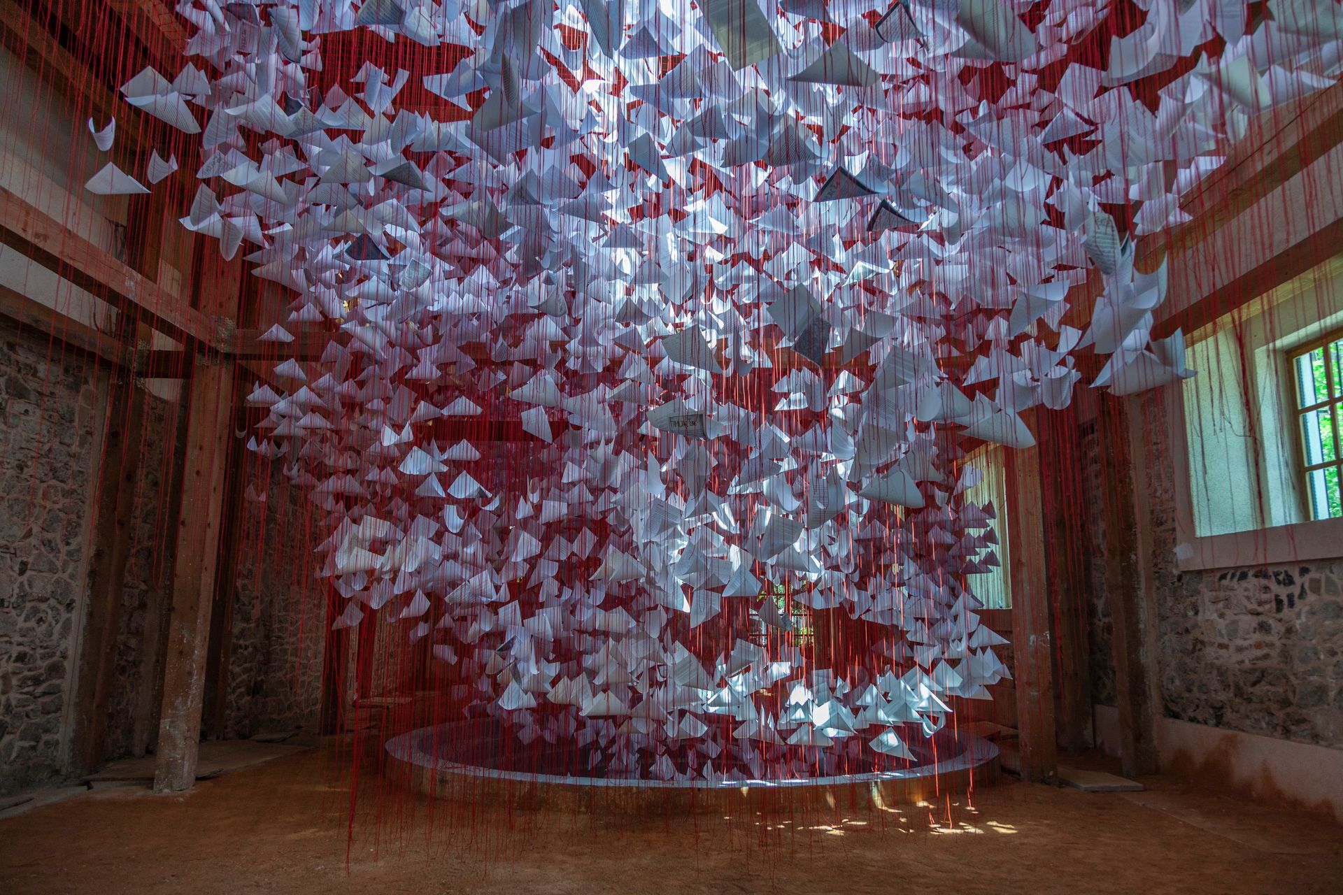 An art installation comprised of sheets of paper suspended by red thread in a room